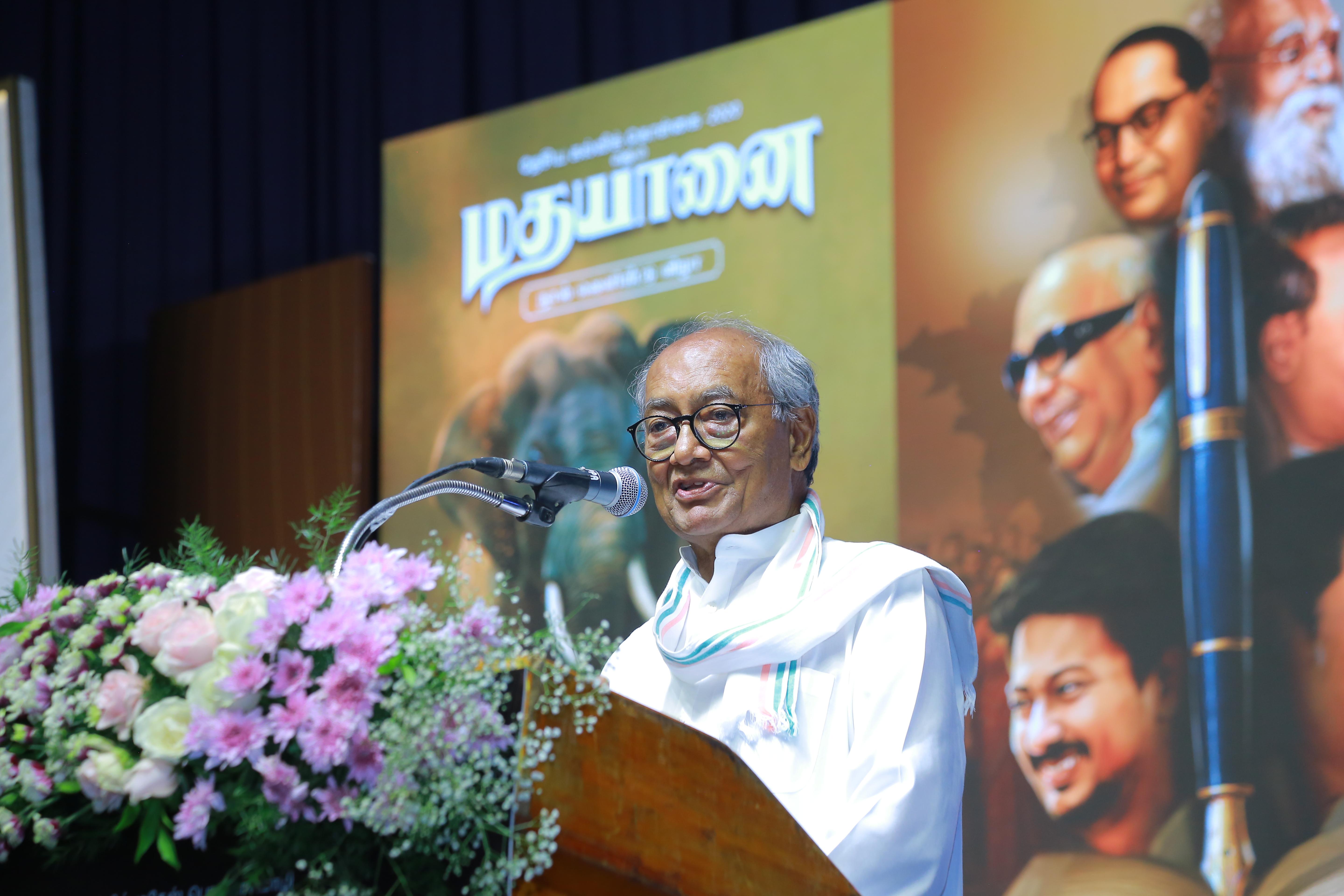 Digvijaya Singh seen reflecting on the stage at the "Madhayaanai" book launch, foregrounded by soft floral hues and symbolic backdrop.