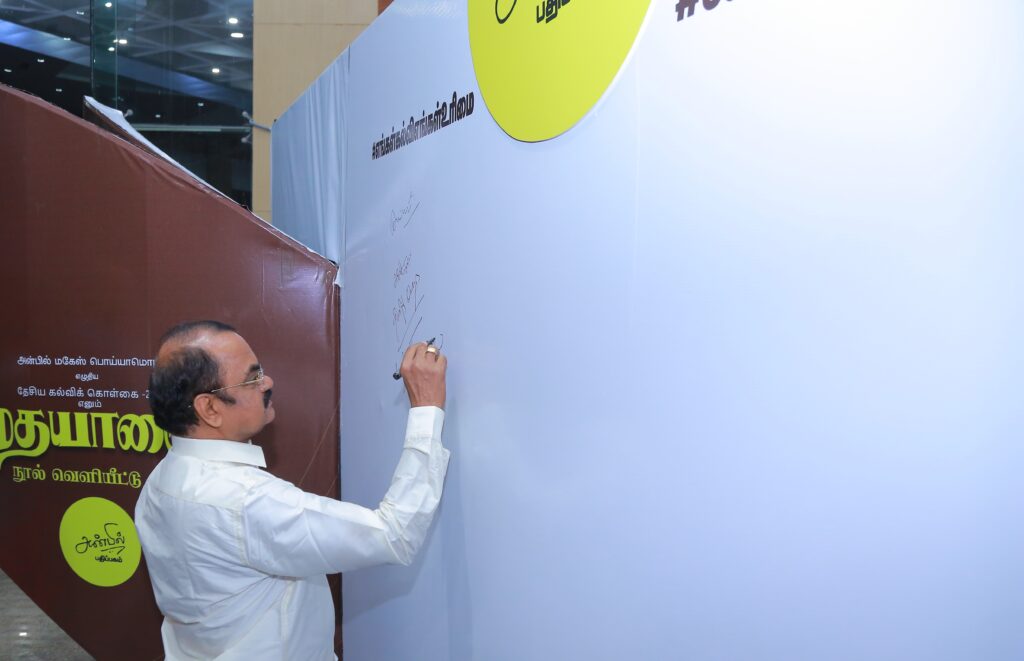 Dr. Mylswamy Annadurai signing the pledge wall during the "Madhayaanai" book release event, supporting educational rights.
